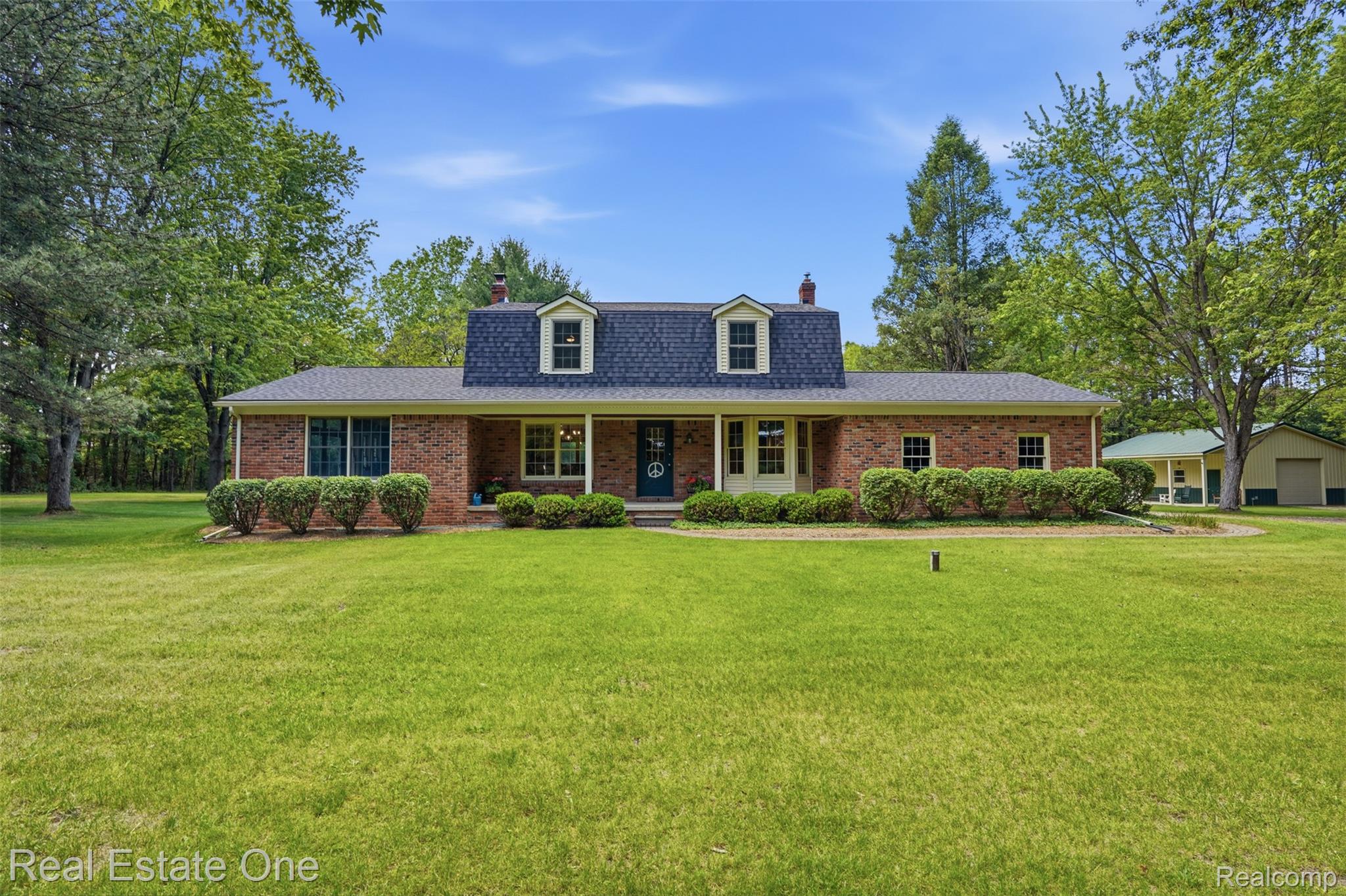 1765 Rowe Road Milford, MI 48380 - Photo 1 of 61 Brick facade residence featuring a covered front porch with white columns, a dark shingle roof, and dormer windows