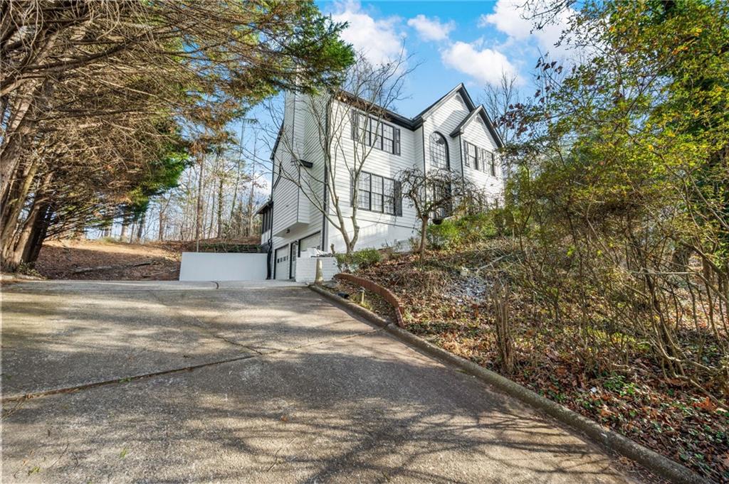 a view of a white house next to a road with large trees