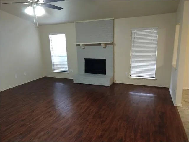 an empty room with wooden floor chandelier fan and windows