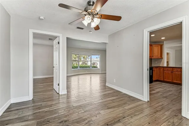 a view of an empty room with wooden floor and a ceiling fan
