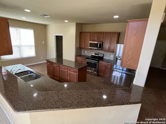 a kitchen with stainless steel appliances granite countertop a sink a stove a refrigerator a washer dryer and a microwave