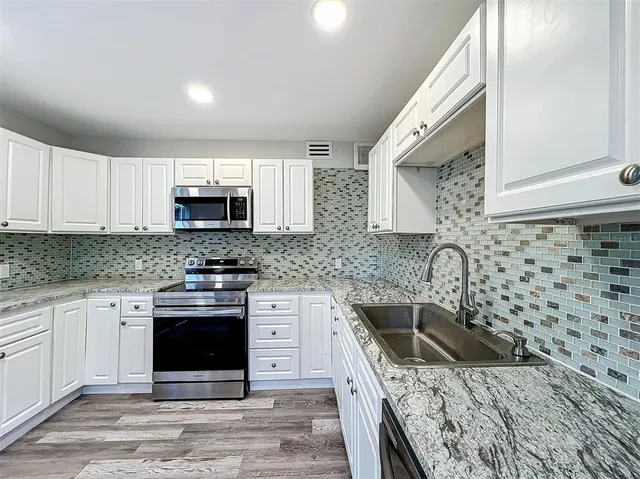 a kitchen with granite countertop white cabinets stainless steel appliances and a sink