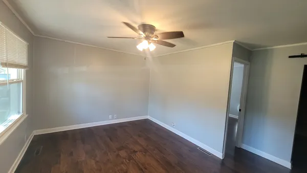 an empty room with wooden floor fan and windows