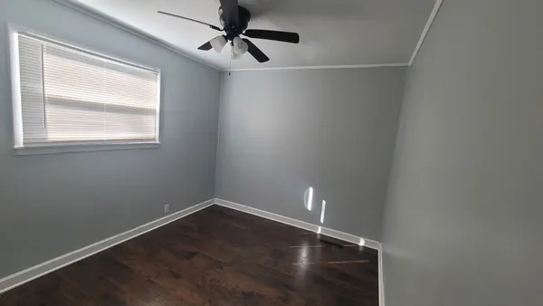 an empty room with wooden floor fan and windows