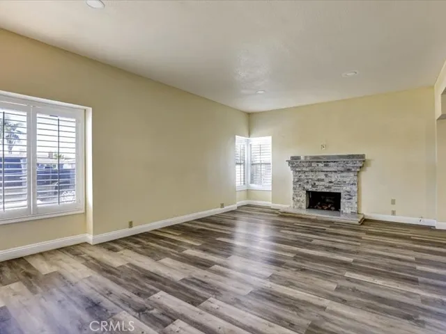 a view of an empty room with wooden floor fireplace and a window