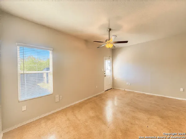 an empty room with a chandelier fan and windows
