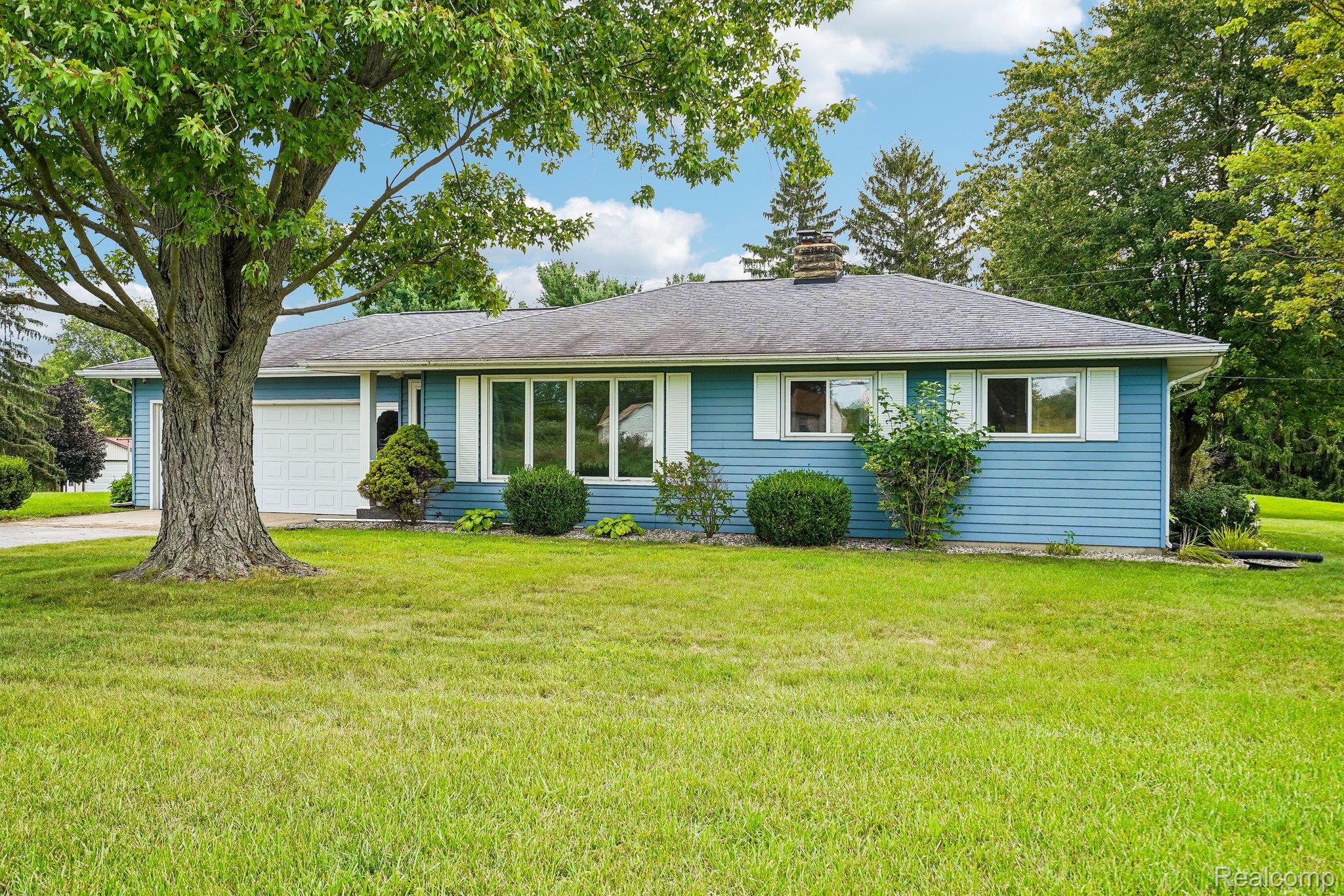 3981 South State Road Durand, MI 48429 - Photo 1 of 33 Ranch-style residence featuring blue horizontal siding, a dark shingled roof, white window trim, and a prominent front-facing garage