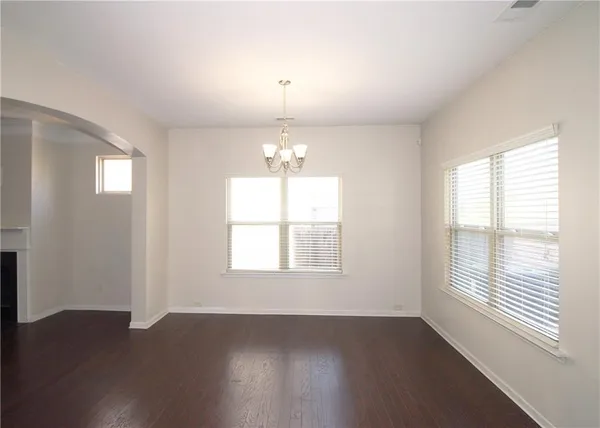 an empty room with wooden floor chandelier and windows