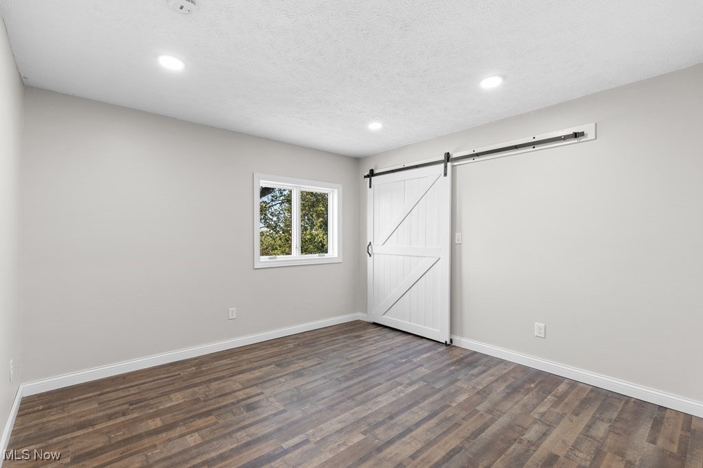 139 Patterson Road Weirton, WV 26062 - Photo 20 of 46 Unfurnished bedroom featuring dark wood finished floors, a barn door, recessed lighting, and a textured ceiling