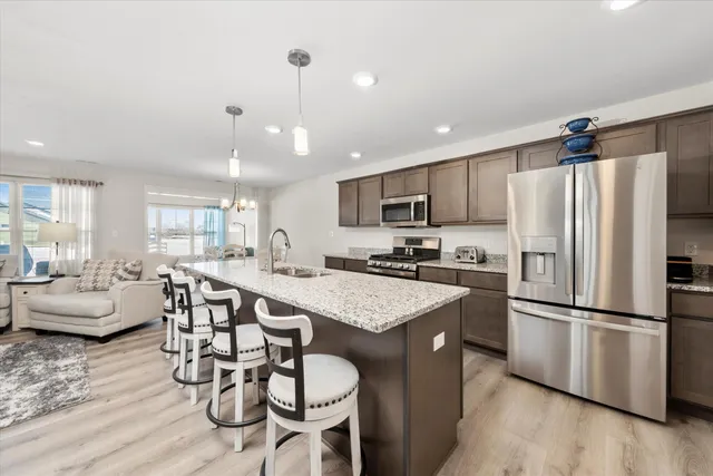 a kitchen with stainless steel appliances granite countertop a refrigerator a stove a sink a dining table and chairs with wooden floor