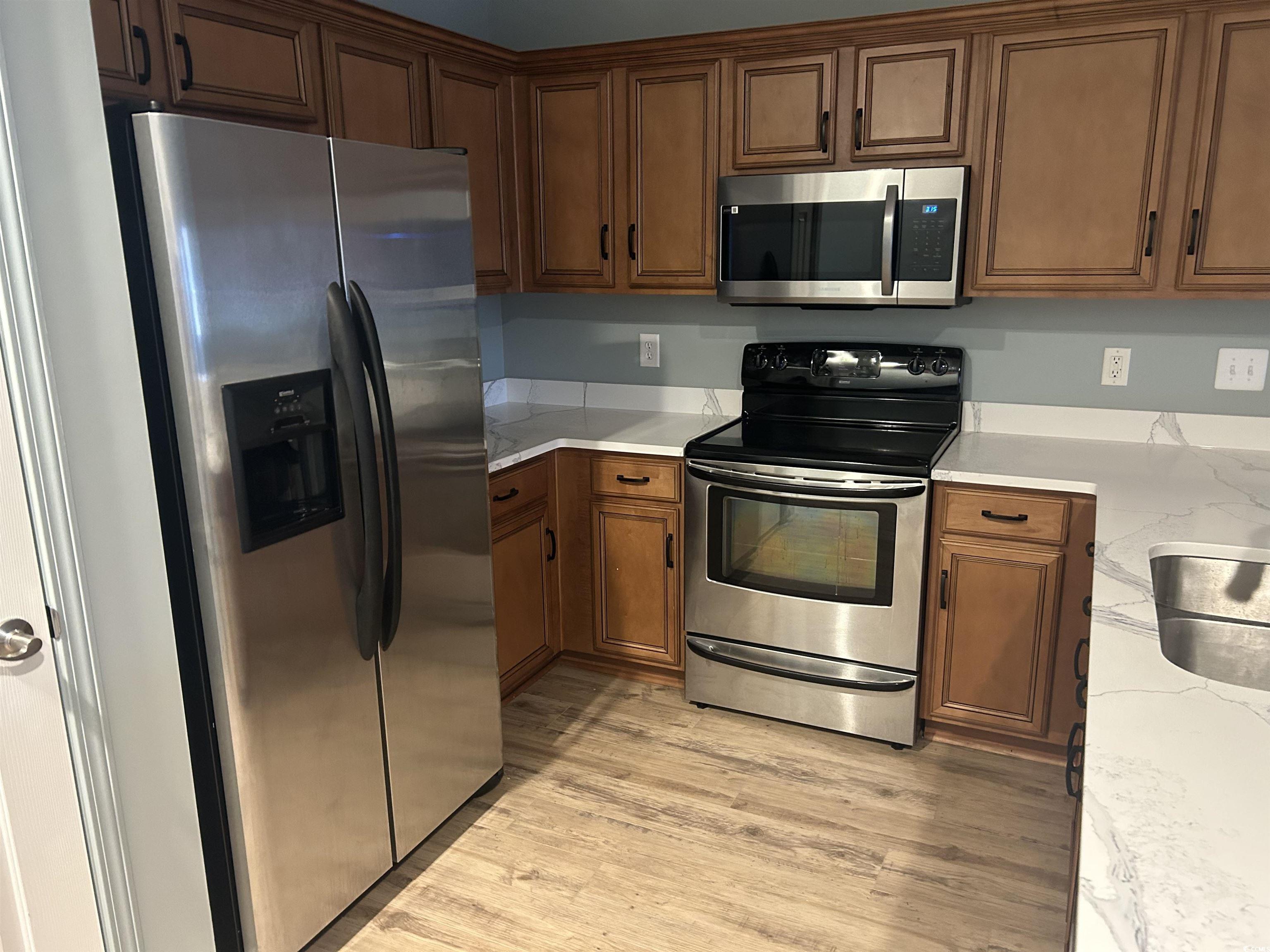 4104 Pinehurst Circle, Unit 2G Little River, SC 29566 - Photo 4 of 17 Kitchen featuring stainless steel appliances, light wood-type flooring, brown cabinets, and light stone counters