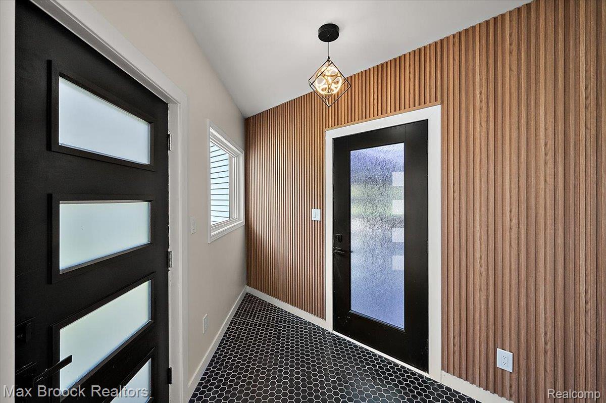 4597 Clarkston Road Clarkston, MI 48348 - Photo 24 of 74 Entryway featuring black hexagonal tile flooring, a slatted wood-finish accent wall, and a modern geometric pendant light fixture