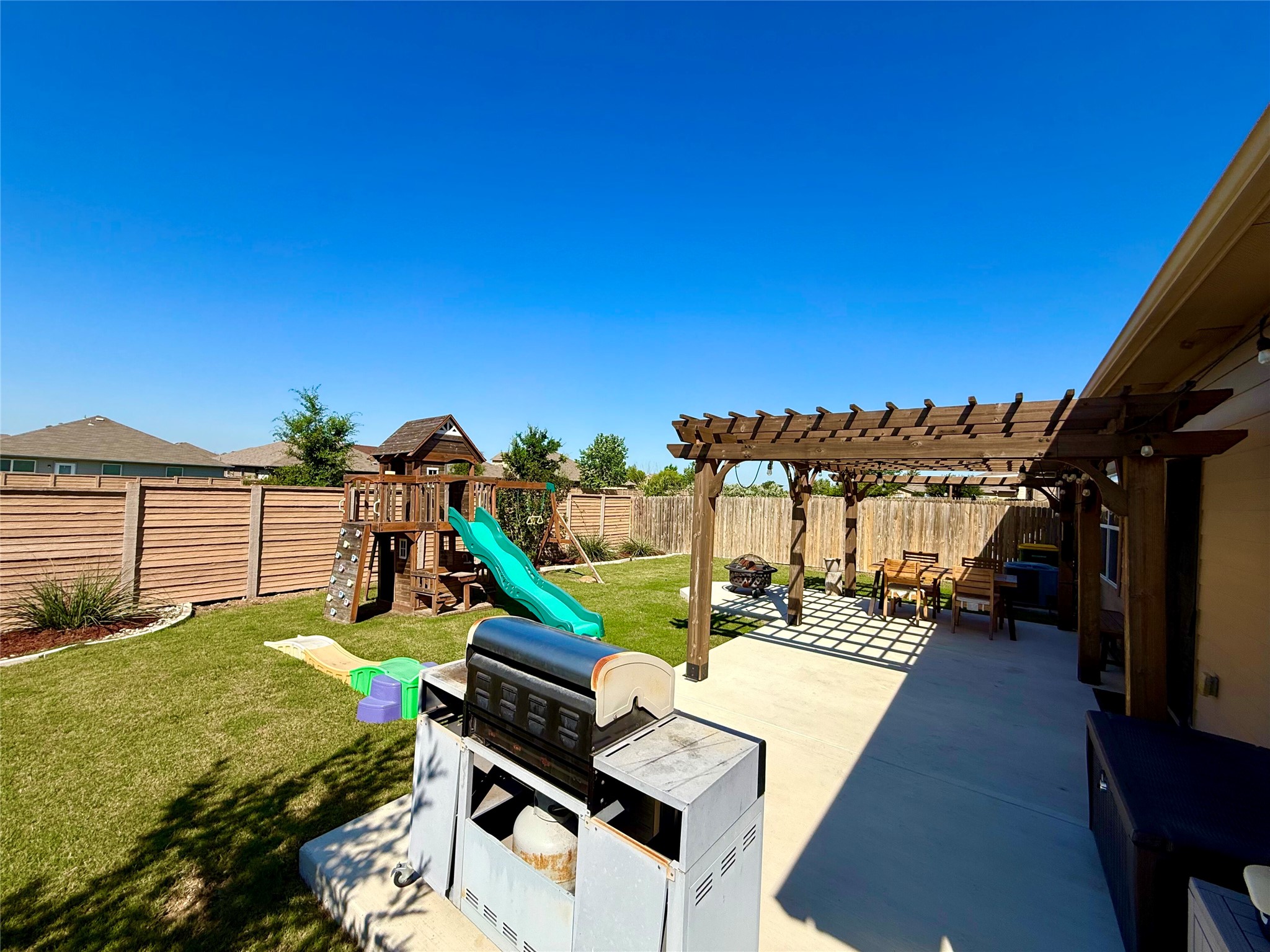 11700 Andesite Road Manor, TX 78653 - Photo 28 of 32 A spacious backyard features a pergola-covered patio for outdoor dining and a dedicated play area for children.
