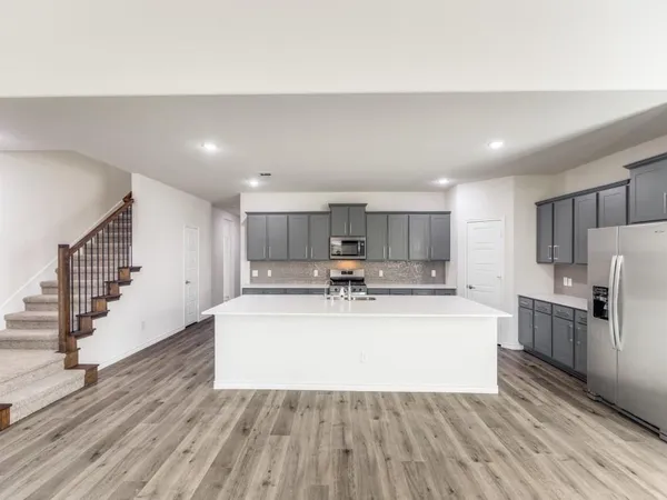 a large white kitchen with a stove a sink dishwasher a refrigerator and white cabinets with wooden floor