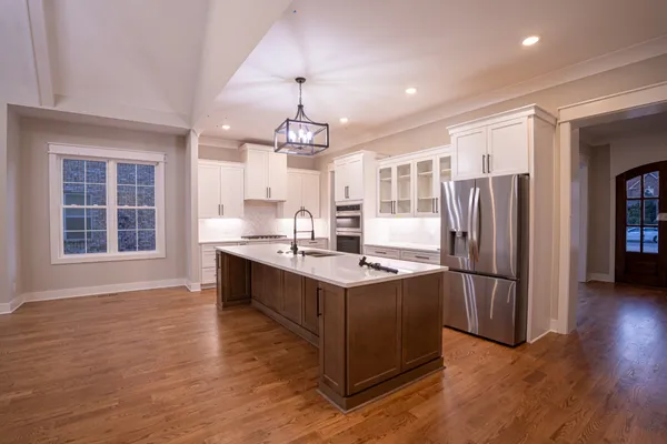 a kitchen with stainless steel appliances granite countertop a refrigerator a sink dishwasher a stove and a dining table with wooden floor