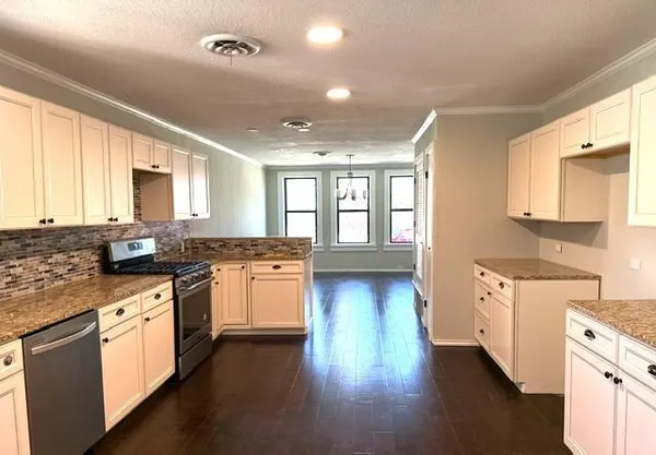 a large kitchen with granite countertop a stove top oven a sink a dining table and chairs with wooden floor