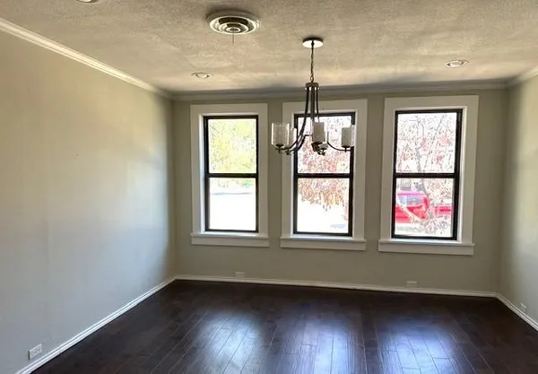 an empty room with wooden floor chandelier and windows