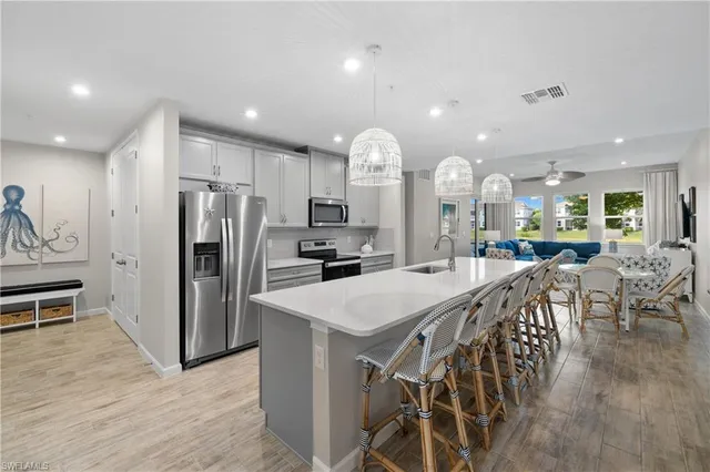 a kitchen with stainless steel appliances kitchen island granite countertop a refrigerator a stove a sink a dining table and chairs with wooden floor