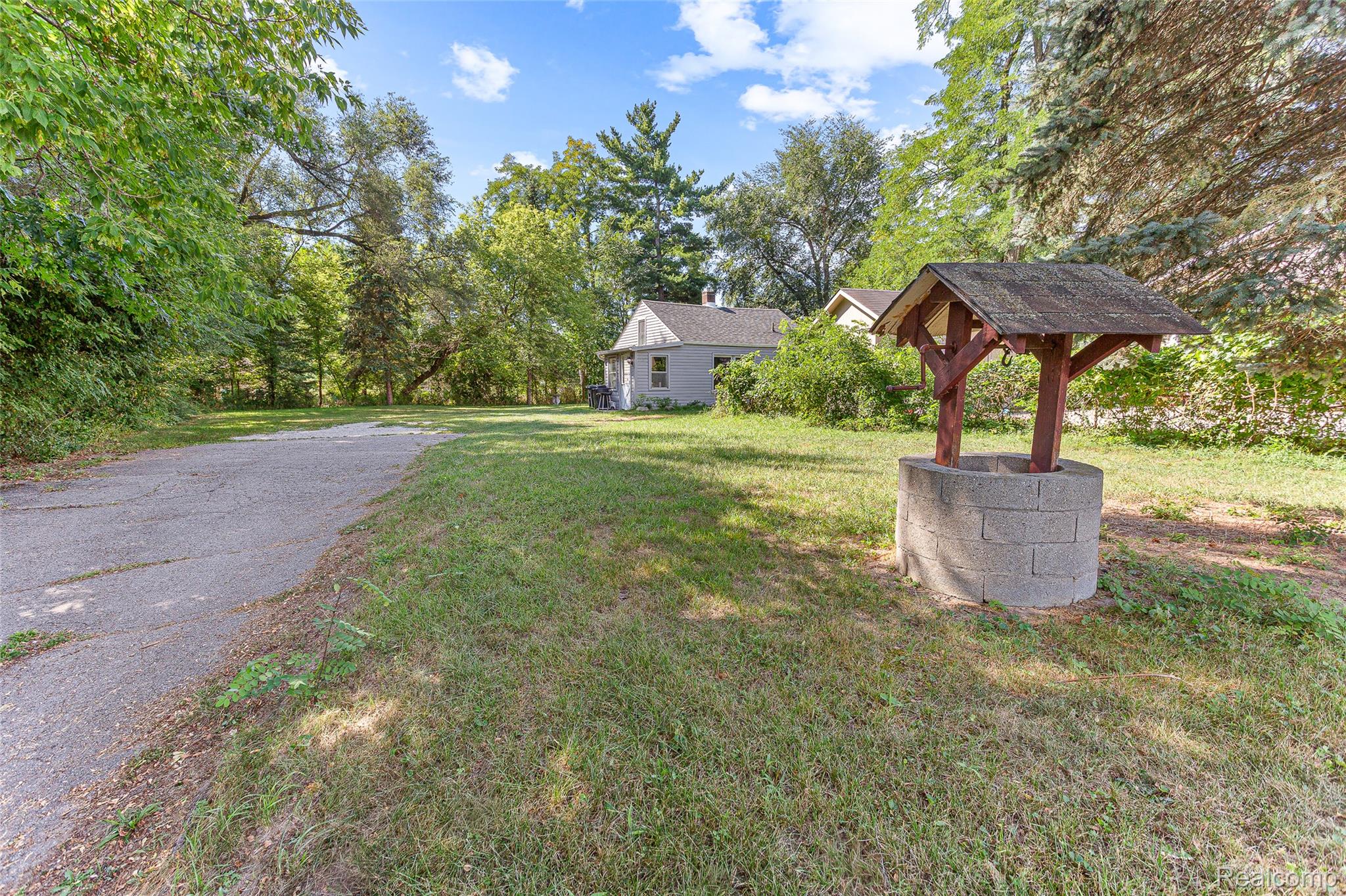2550 Loon Lake Road Wixom, MI 48393 - Photo 9 of 36 Expansive green space featuring a decorative well with a wooden canopy, mature trees, and a paved drive
