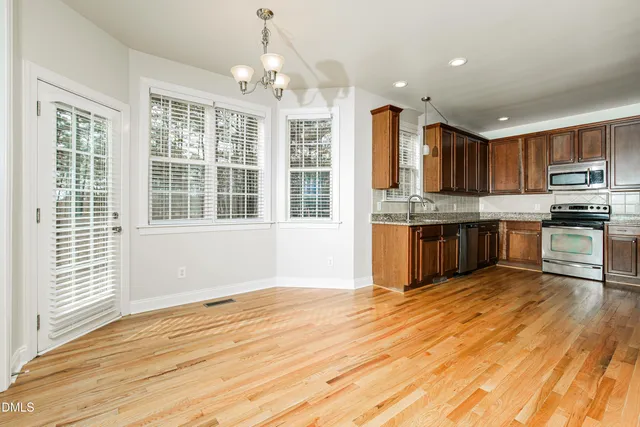 a kitchen with stainless steel appliances granite countertop a stove top oven a sink dishwasher a dining table and chairs with wooden floor