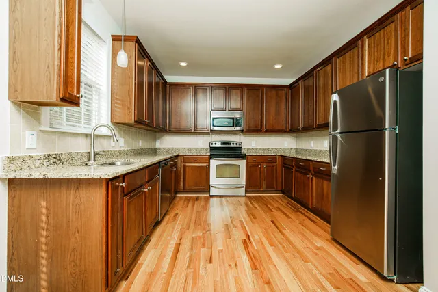 a kitchen with kitchen island granite countertop wooden floors stainless steel appliances a sink and a window