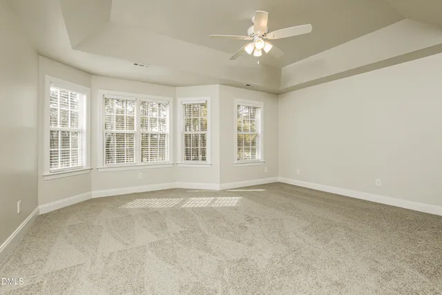 an empty room with chandelier fan and windows