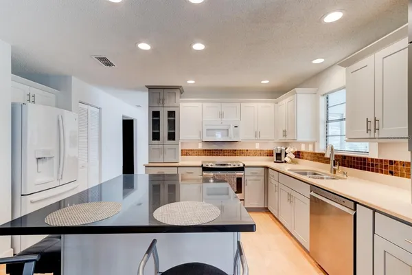 a kitchen with stainless steel appliances granite countertop a sink a stove a refrigerator cabinets and chairs