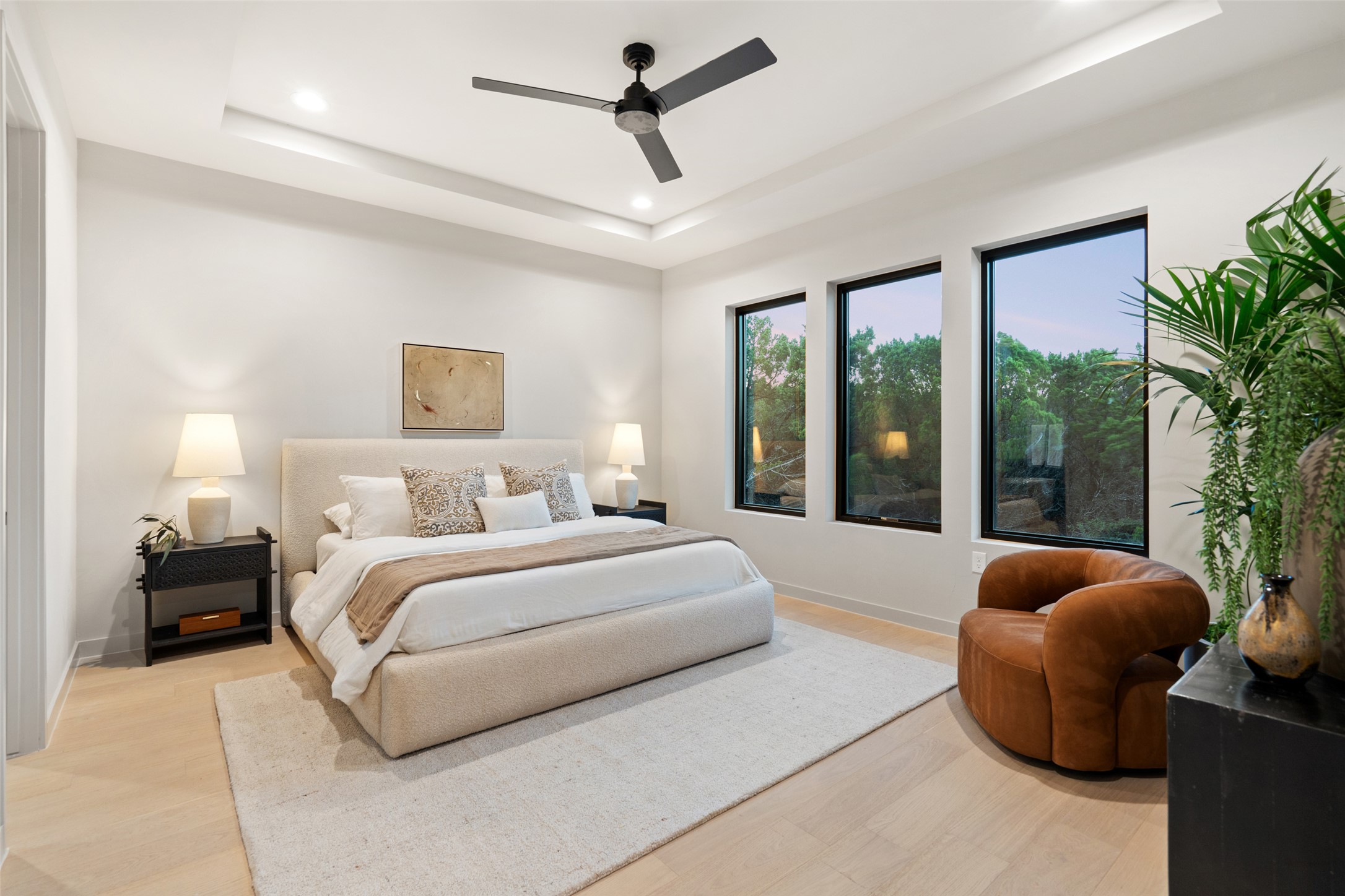 9803 Ribelin Ranch Court, Unit 19 Austin, TX 78750 - Photo 5 of 14 A tranquil primary bedroom features light wood flooring, a decorative tray ceiling, and large windows framing lush outdoor views.