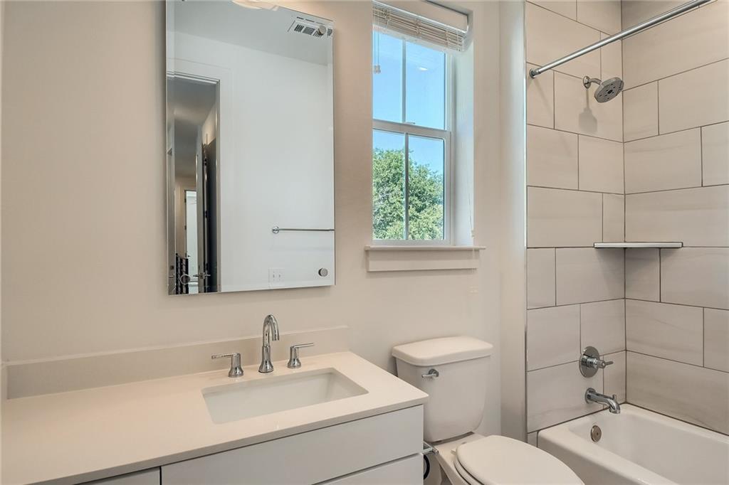 2624 Metcalfe Road, Unit 7 Austin, TX 78741 - Photo 25 of 31 Modern bathroom featuring a rectangular vanity sink with a chrome faucet, a large vanity mirror, a window with natural light, a toilet, and a tiled shower-tub combination with a built-in shelf