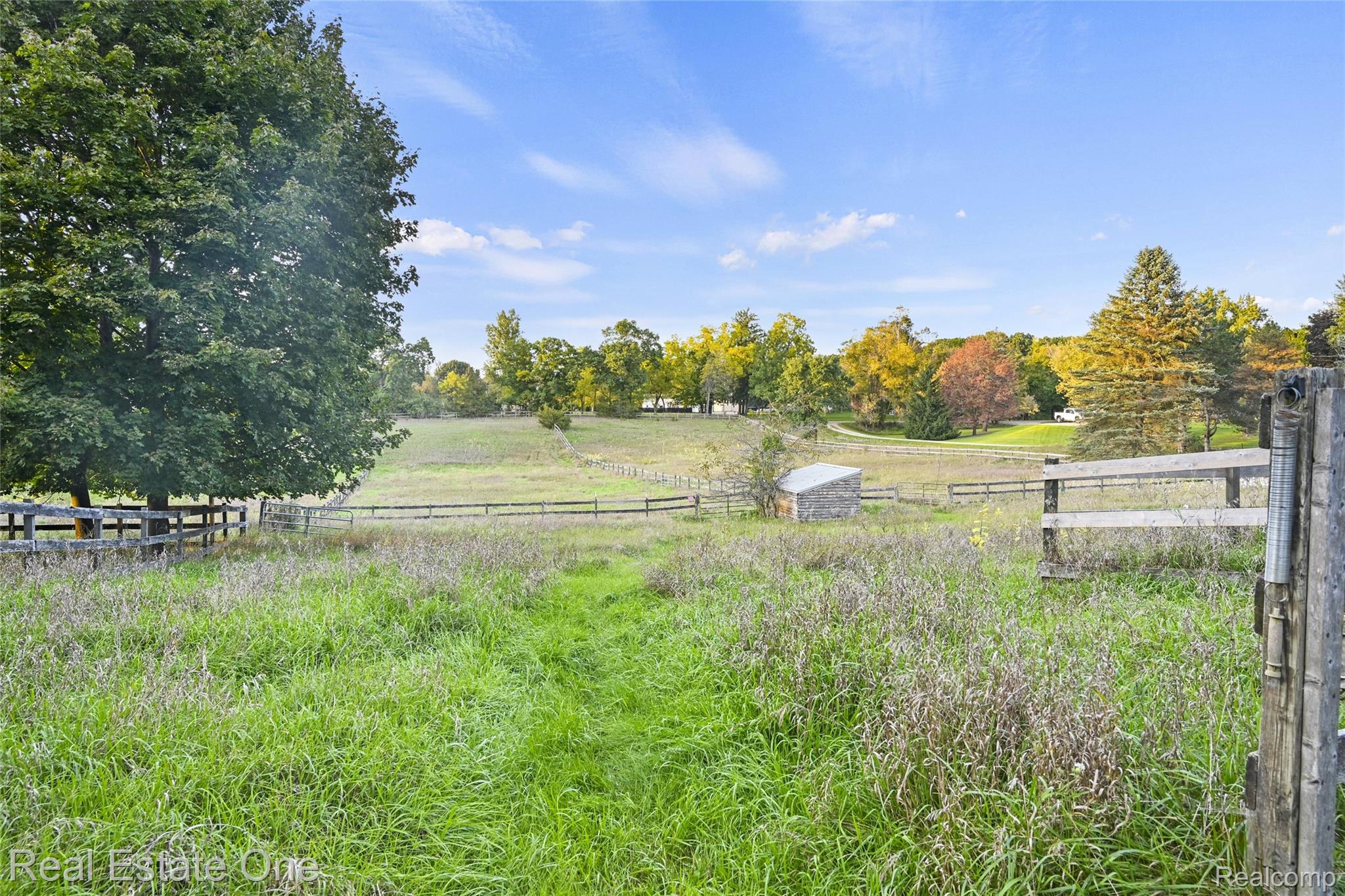 895 Rowe Road Milford, MI 48380 - Photo 21 of 50 Expansive grassy field with a wooden fence boundary, mature trees, and a small utility shed