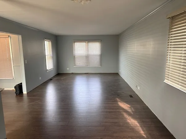an empty room with wooden floor and windows with curtains