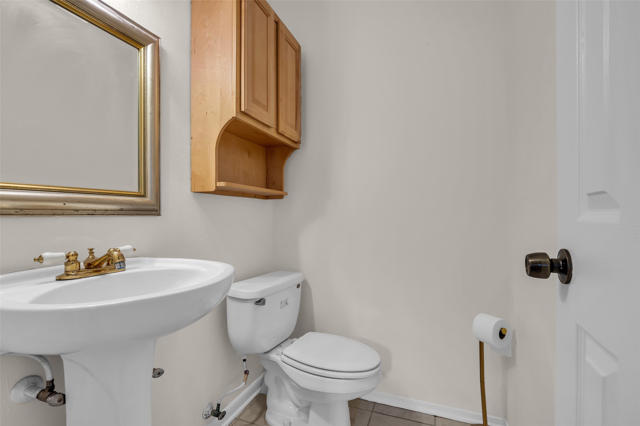 1447 Silverpines Road Houston, TX 77062 - Photo 7 of 17 Conveniently located for guests, this well-appointed half bath features a pedestal sink with brass fixtures, a large mirror, and a wall-mounted wooden cabinet that provides additional storage while maintaining a clean and functional design. Its thoughtful location and classic finishes make it a practical addition to the home.