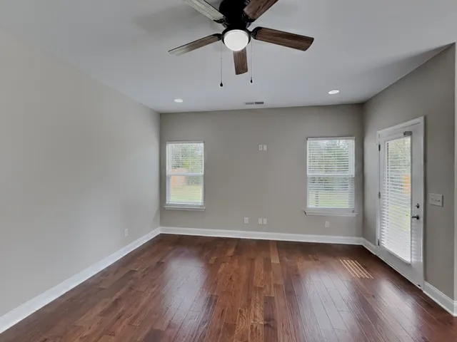 an empty room with wooden floor a ceiling fan and windows