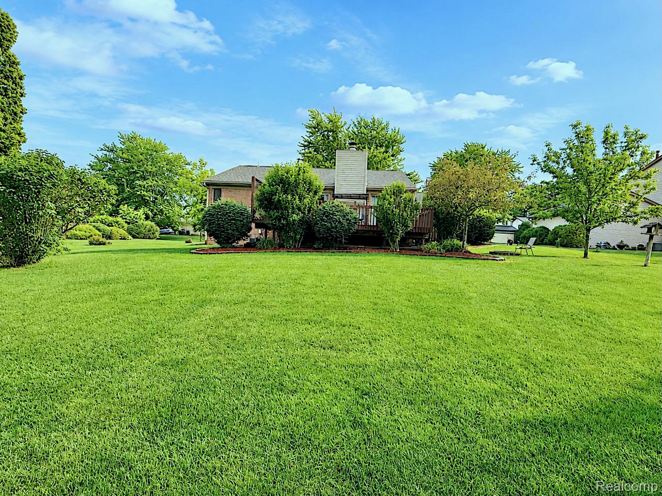 2033 Avonstoke Road Rochester, MI 48307 - Photo 24 of 27 Expansive green lawn with established landscaping surrounding a rear wood deck and brick exterior