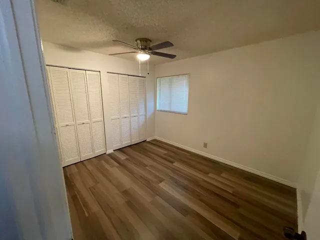 an empty room with wooden floor fan and windows