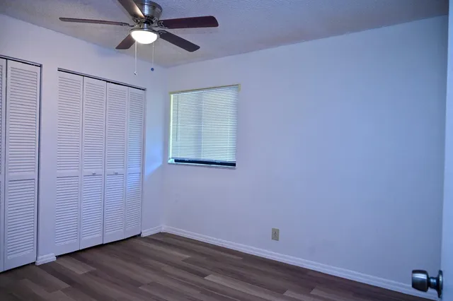 a view of an empty room with wooden floor and a ceiling fan