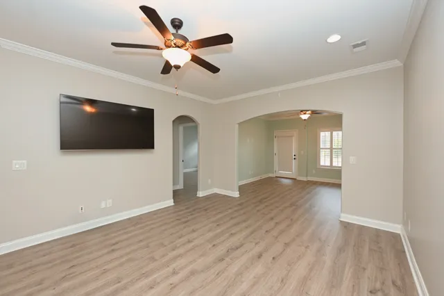 a view of an empty room with wooden floor and a ceiling fan