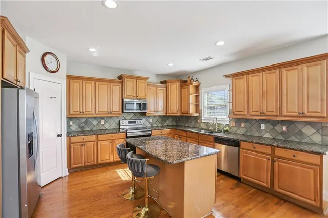 a kitchen with stainless steel appliances granite countertop a stove a sink dishwasher and a refrigerator with wooden floor