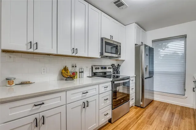 a kitchen with stainless steel appliances granite countertop white cabinets a stove a sink and dishwasher with wooden floor