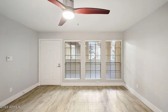 an empty room with wooden floor fan and windows