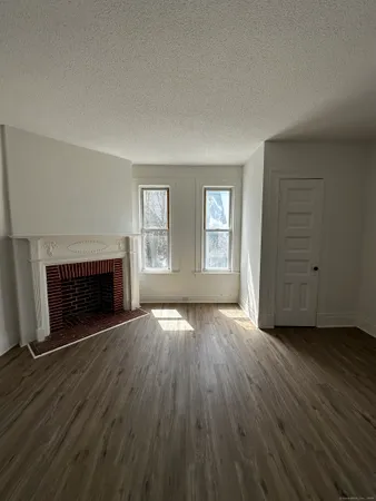 an empty room with wooden floor fireplace and windows