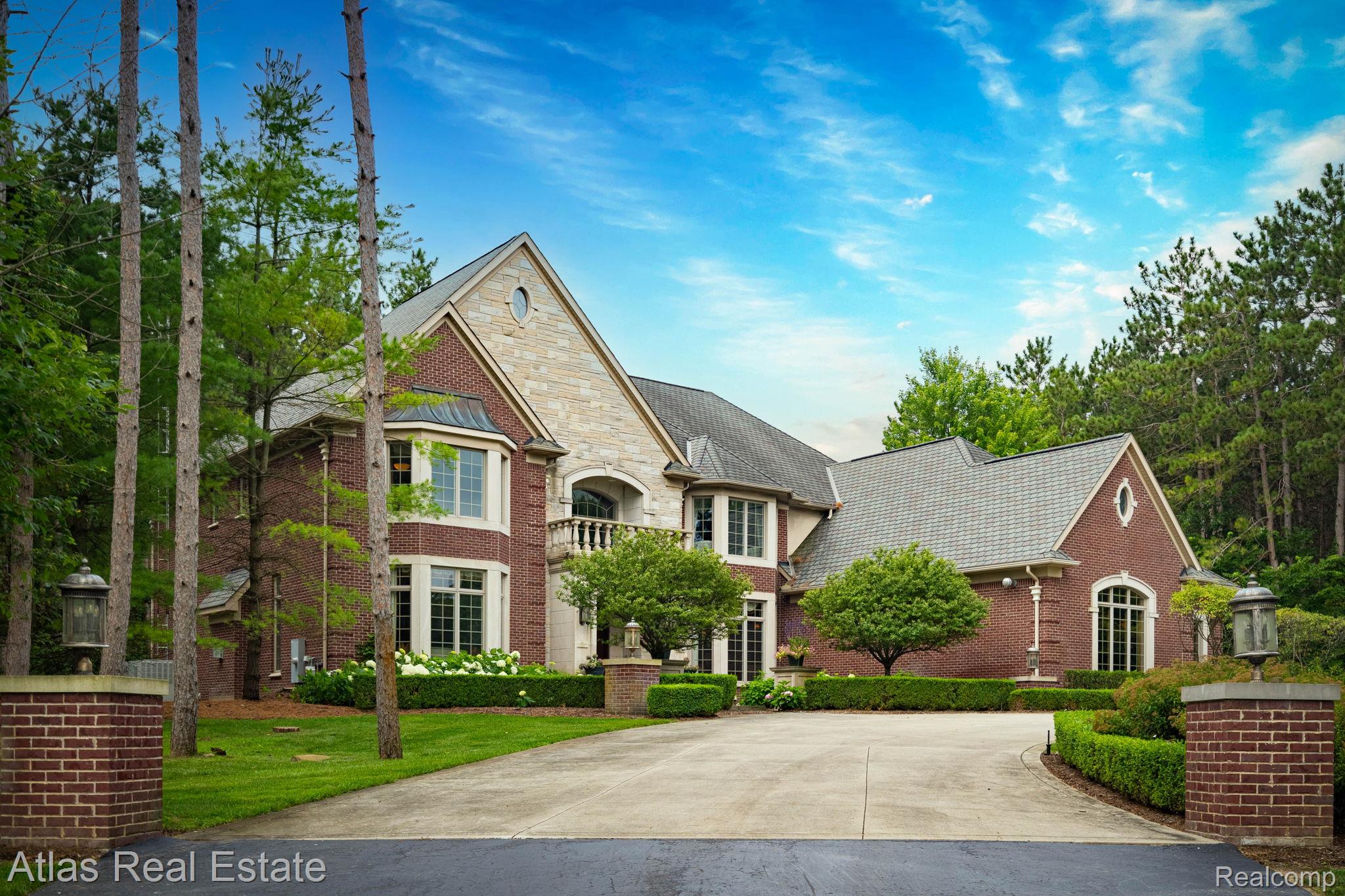 Brick and stone facade residence featuring a paved driveway, manicured landscaping, mature trees, and classic exterior lighting