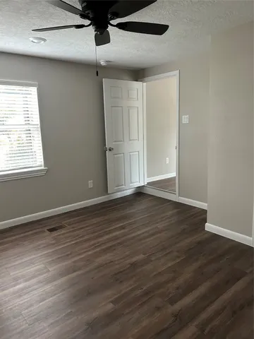 an empty room with wooden floor chandelier fan and windows