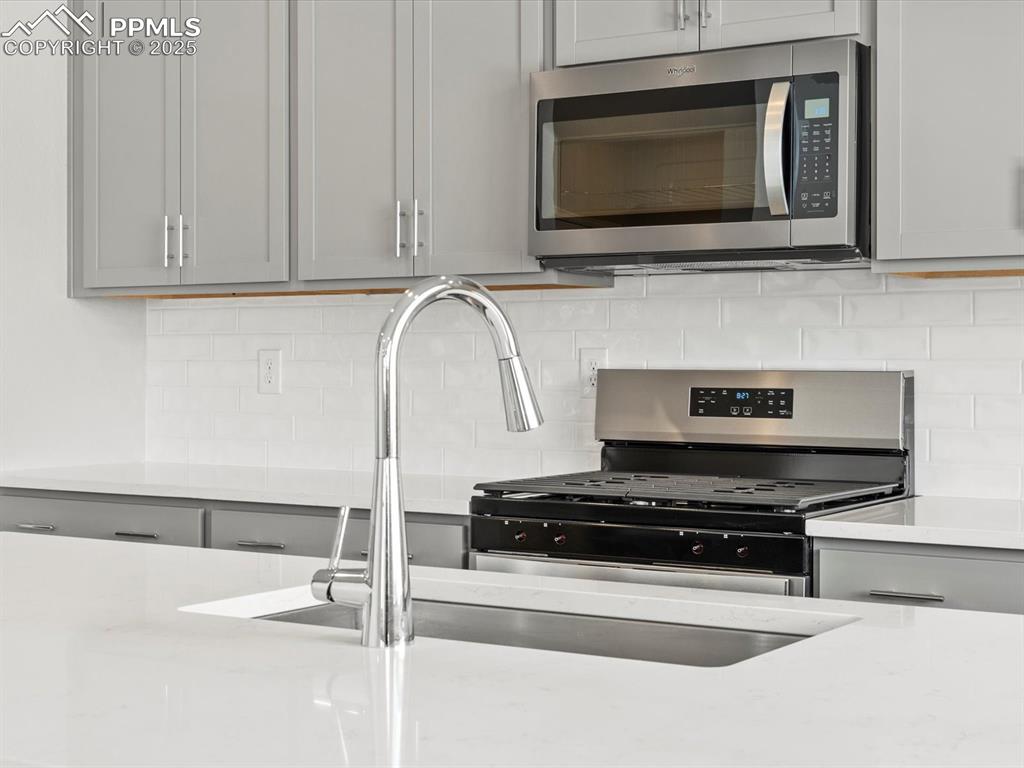 10636 Waterloo Drive Peyton, CO 80831 - Photo 11 of 36 Kitchen featuring a sink, stainless steel microwave, backsplash, and gray cabinetry