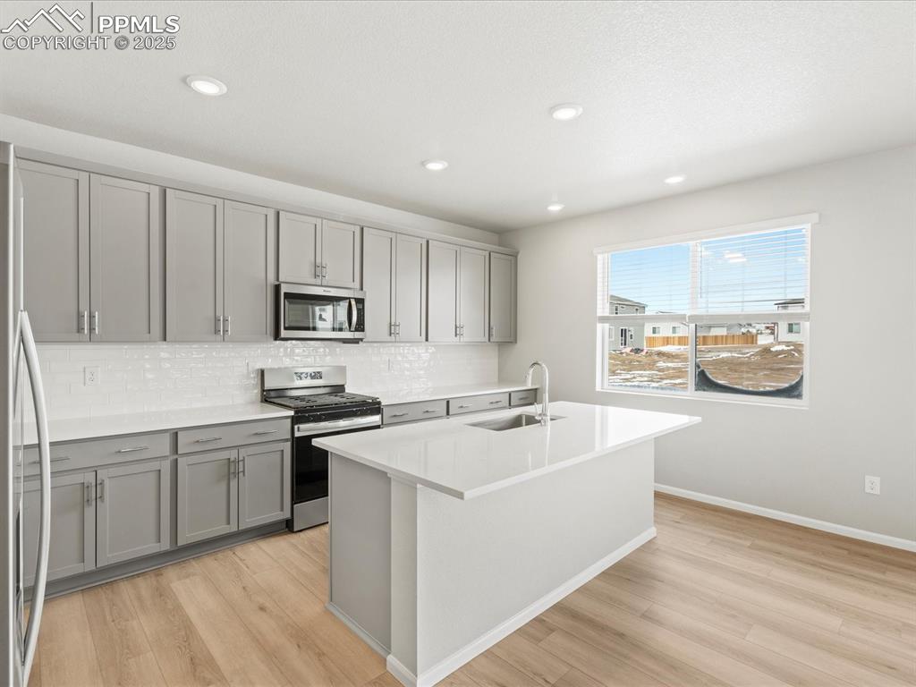 10636 Waterloo Drive Peyton, CO 80831 - Photo 2 of 36 Kitchen featuring gray cabinetry, a sink, tasteful backsplash, appliances with stainless steel finishes, and light wood finished floors