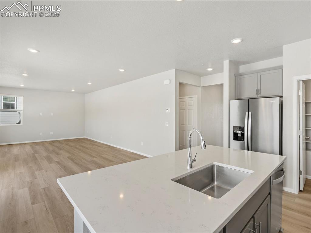 10636 Waterloo Drive Peyton, CO 80831 - Photo 6 of 36 Kitchen with light wood finished floors, gray cabinetry, light stone countertops, stainless steel refrigerator with ice dispenser, and a sink