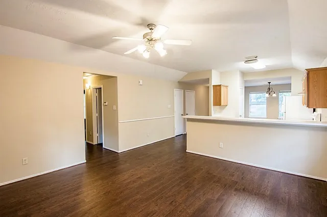 a view of an empty room with wooden floor and a kitchen