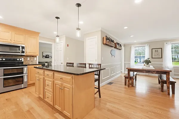 a kitchen with stainless steel appliances granite countertop a stove top oven a sink a dining table and chairs with wooden floor