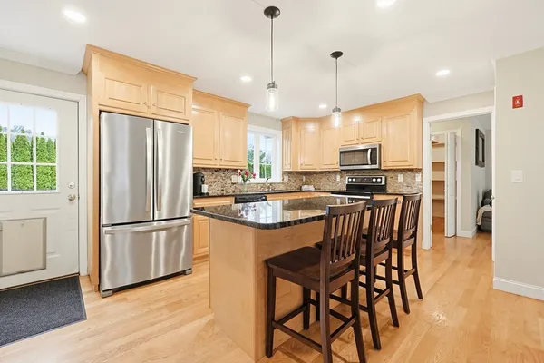 a kitchen with stainless steel appliances granite countertop a refrigerator a stove a sink a dining table and chairs with wooden floor