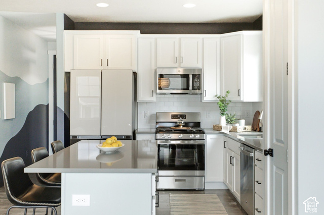 986 South Old Farm Road Heber City, UT 84032 - Photo 16 of 51 Modern kitchen featuring white cabinetry, stainless steel appliances, a subway tile backsplash, a kitchen island with seating, and wood-finish flooring